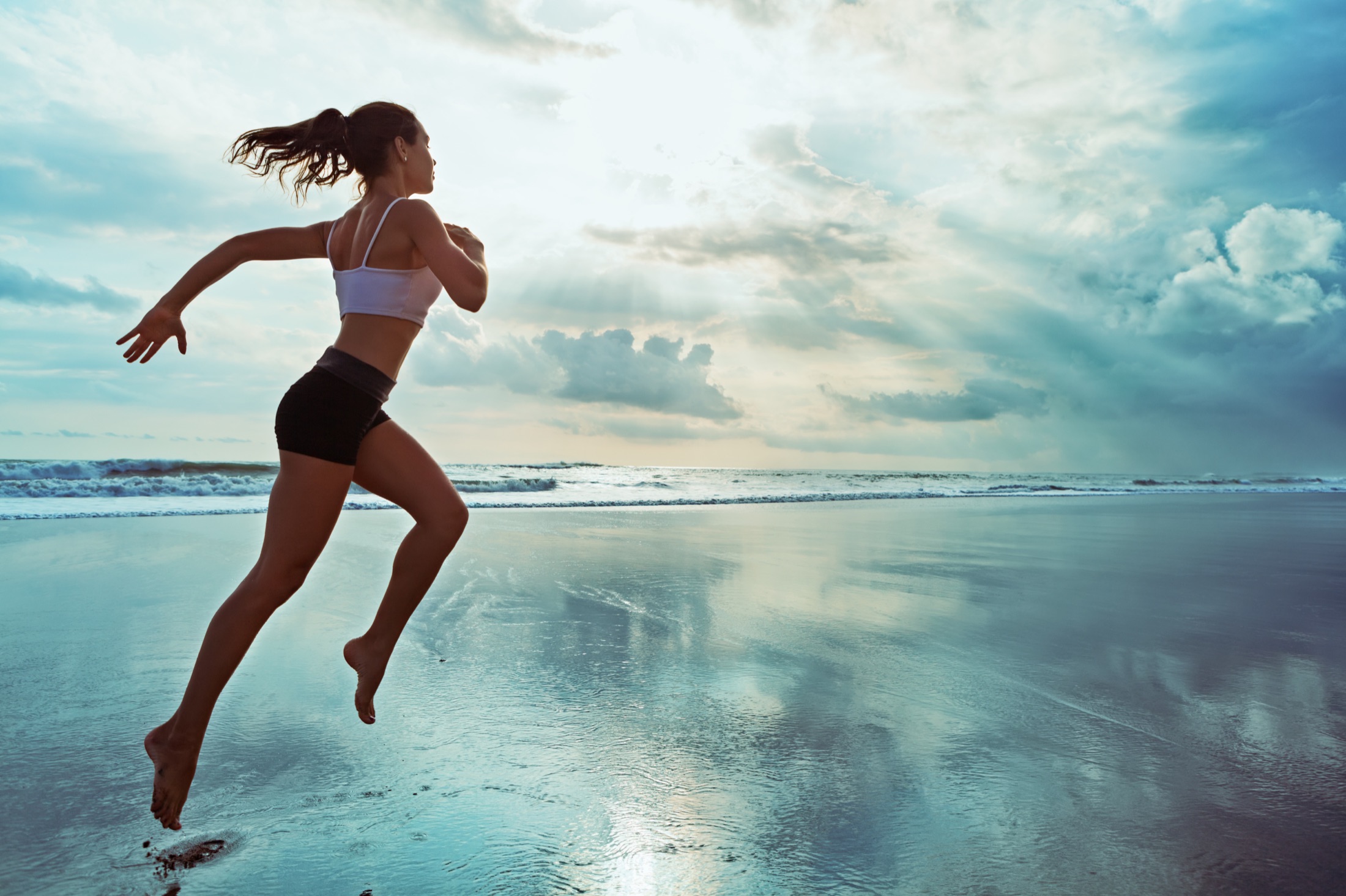 Runner moving along a beach beneath an open sky
